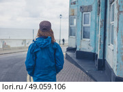 A young woman is standing in the street outside a blue house by the coast on a windy day. Стоковое фото, агентство Ingram Publishing / Фотобанк Лори