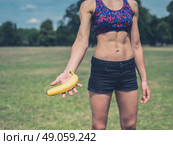 A fit young woman is standing in a park and is offering a banana. Стоковое фото, агентство Ingram Publishing / Фотобанк Лори