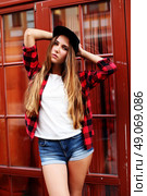 Lifestyle portrait of fashionable blonde girl with ombre hair wearing a rock red shirt, black cap, white t-shirt and denim shorts having fun outdoors in the city. Swag style. Стоковое фото, агентство Ingram Publishing / Фотобанк Лори