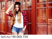 Lifestyle portrait of fashionable blonde girl with ombre hair wearing a rock red shirt, black cap, white t-shirt and denim shorts having fun outdoors in the city. Swag style. Стоковое фото, агентство Ingram Publishing / Фотобанк Лори