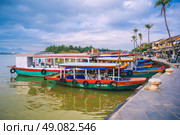 Traditional wooden Vietnamese boats on the Thu Bon River in the old town in Hoi An in Vietnam. Vietnam, Hoi An - December 1, 2024. Редакционное фото, фотограф Корчагина Анастасия / Фотобанк Лори