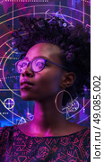 A young woman with glasses and hoop earrings gazes upwards, lit by a vibrant pink and purple light emanating from a digital pattern behind her. Стоковое AI-изображение, AI-художник Данила Большаков / Фотобанк Лори