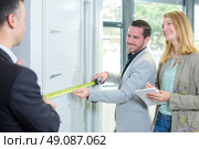 Couple measuring a door, salesman helping. Стоковое фото, агентство Ingram Publishing / Фотобанк Лори