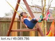 Kid toddler girl swinging on a playground swing in the backyard latin ethnicity. Стоковое фото, агентство Ingram Publishing / Фотобанк Лори