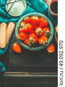 Strawberries for tiramisu making. Ripe strawberries in blue bowl with tiramisu  cooking ingredients on old dark wooden background, top view, place for text. Italian food concept. Стоковое фото, агентство Ingram Publishing / Фотобанк Лори