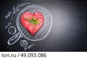 Heart shaped chop of meat on black chalkboard with  painted pan and ingredients, top view, place for text. For Meat lovers and eater. Стоковое фото, агентство Ingram Publishing / Фотобанк Лори