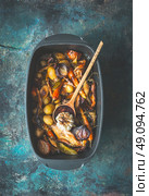 Very rustic roasted vegetables stew or ragout with wild game and wild fowl and forest mushrooms in black backing dish with wooden cooking spoon on dark aged background, top view. Country food. Стоковое фото, агентство Ingram Publishing / Фотобанк Лори