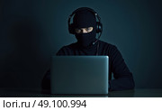 Мужчина в маске балаклаве и с гарнитурой за ноутбуком. Стоковое AI-изображение, AI-художник Илья Старков / Фотобанк Лори