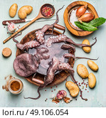 Raw octopus in pan with water and ingredients for cooking: potatoes with spices on rustic wooden table. Top view. Spanish kitchen. Стоковое фото, агентство Ingram Publishing / Фотобанк Лори