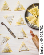 Fresh triangular ravioli with kitchen tools on white wooden background, top view. Стоковое фото, агентство Ingram Publishing / Фотобанк Лори