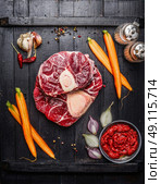 Raw veal shank slices meat and ingredients for Osso Buco cooking on black wooden background, top view. Стоковое фото, агентство Ingram Publishing / Фотобанк Лори