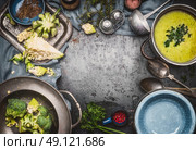 Green Romanesco and broccoli soup with cooking ingredients,kitchen tools, ladle , bowls and spoons on dark rustic background, top view, frame. Healthy and vegetarian food or diet nutrition concept. Стоковое фото, агентство Ingram Publishing / Фотобанк Лори