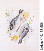 two raw dorado fish with lemon, spices and spoon on paper, composing on white wooden background, top view. Стоковое фото, агентство Ingram Publishing / Фотобанк Лори
