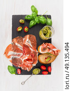 prosciutto ham with bread, basil pesto and tomatoes on slate and white wooden background, top view. Стоковое фото, агентство Ingram Publishing / Фотобанк Лори