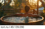 A man enjoying a soak in a hot tub situated on a wooden deck, surrounded by a serene outdoor setting. Стоковое AI-изображение, AI-художник Данила Большаков / Фотобанк Лори
