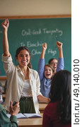 A woman in a classroom raises her right arm in a fist pump as celebrating successful graduation of her students. cheer for her innovative teaching method. Beginning school vacations. Стоковое AI-видео, аниматор Sergey Grishin / Фотобанк Лори