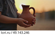 A child's small hands holding a clay water jug, symbolizing the thirst of Imam Hussain family, under the fading light of sunset. Стоковое AI-видео, аниматор Sergey Grishin / Фотобанк Лори