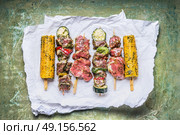 Various Meat Skewers  for grill with vegetables , corn ears and condiment on green rustic background , top view. Стоковое фото, агентство Ingram Publishing / Фотобанк Лори