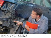 Mechanic holding clipboard assessing car. Стоковое фото, агентство Ingram Publishing / Фотобанк Лори