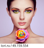 Portrait of beautiful young woman with rainbow rose. Bright colors. Long eyelashes, vivid colorful eyeshadows. Rainbow make up. Multicolored flowers. Стоковое фото, агентство Ingram Publishing / Фотобанк Лори