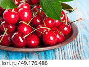 Red sweet cherry and green leaves in a clay dish on a blue wooden background. Стоковое фото, агентство Ingram Publishing / Фотобанк Лори