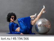 Spectacular Woman in a sparkly flared suit and afro wig poses with a disco ball. Disco style from the seventies or eighties. Стоковое фото, фотограф Лазаренко Светлана / Фотобанк Лори