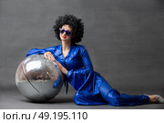 Spectacular Woman in a sparkly flared suit and afro wig poses with a disco ball. Disco style from the seventies or eighties. Стоковое фото, фотограф Лазаренко Светлана / Фотобанк Лори