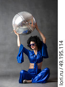A woman in a seventies flared suit with a disco ball in an afro wig on a gray background. Стоковое фото, фотограф Лазаренко Светлана / Фотобанк Лори
