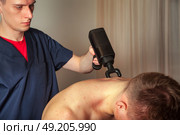 Sports Massage Session Featuring Percussion Massager on Client in Indoor Setting. Стоковое фото, фотограф Aleksandr Golubev / Фотобанк Лори