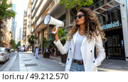 A woman stands on a bustling city street, holding a megaphone and speaking loudly to the crowd. Стоковое AI-изображение, AI-художник Данила Большаков / Фотобанк Лори
