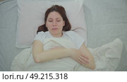 Young adult woman lies in bed in the morning and rubs her hand, who is numb after sleeping in an uncomfortable position. Стоковое видео, видеограф Денис Кебедов / Фотобанк Лори