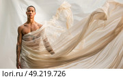 Young man with tattoos on his body is standing in front of a white sheet. Стоковое AI-изображение, AI-художник Данила Большаков / Фотобанк Лори