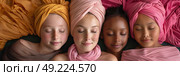 Four young women with eyes closed, heads touching, draped in vibrant headscarves, conveying peace and diversity. Стоковое AI-изображение, AI-художник Данила Большаков / Фотобанк Лори