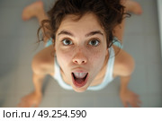 A woman contorts her face into a funny expression as she lies on the floor. Стоковое AI-изображение, AI-художник Данила Большаков / Фотобанк Лори