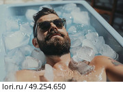 A man wearing sunglasses is lying in a bathtub filled with ice cubes. Стоковое AI-изображение, AI-художник Данила Большаков / Фотобанк Лори