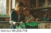A woman and a child are sorting recyclables in a kitchen, placing items into a recycling bin. They are engaged in environmentally-friendly practices. Стоковое AI-изображение, AI-художник Данила Большаков / Фотобанк Лори
