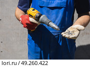 A man in a blue jumpsuit holds electric screwdriver with a riveter attachment and exhaust construction rivets on the background of a slate wall. Стоковое фото, фотограф Неведицына Елена / Фотобанк Лори