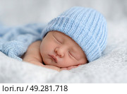 A baby is sleeping with a blue knit hat on. Стоковое AI-изображение, AI-художник Ярославский Максим / Фотобанк Лори