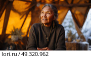 Indigenous elder telling stories inside a warm tent, frost on the outside wall. Life in permafrost conditions, climate change problems on the planet. Global warming. Стоковое AI-изображение, AI-художник ALLA YURTAYEVA / Фотобанк Лори
