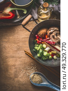 Wok pot with vegetarian asian cuisine ingredients for stir fry with chopped vegetables, spices, sesame seeds and chopsticks on rustic wooden background, top view. Chinese or Thai food cooking concept. Стоковое фото, агентство Ingram Publishing / Фотобанк Лори