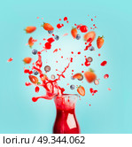 Red juice or smoothie drink is poured out of glass bottle with splash and berries ingredients on turquoise background, front view. Healthy summer beverage concept. Стоковое фото, агентство Ingram Publishing / Фотобанк Лори