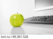 The green apple is on a table on a background of the keyboard and the monitor. Healthy work. Стоковое фото, агентство Ingram Publishing / Фотобанк Лори