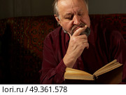The Elderly man it is keen by reading of the book on a dark background. Wise man behind reading by the book. Стоковое фото, агентство Ingram Publishing / Фотобанк Лори