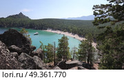 View from the mountain of the bay with turquoise water and sandy beach of Lake Baikal surrounded by pine forest, yachts on the shore. Стоковое видео, видеограф Виктория Тельминова / Фотобанк Лори