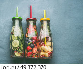 Variety of colorful infused water in bottles with fruits berries, cucumber, herbs and drink straws on gray background, top view. Tasty summer clean beverages for  healthy lifestyle and fitness. Стоковое фото, агентство Ingram Publishing / Фотобанк Лори