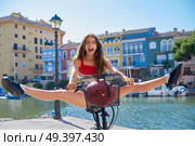 Acrobatic girl riding a bike in a Mediterranean marina port open split legs. Стоковое фото, агентство Ingram Publishing / Фотобанк Лори
