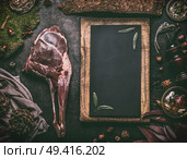Raw aged leg of venison with bone on dark kitchen table with ingredients and  blank chalkboard background for your recipe text, top view. Raw meat leg of deer. Cooking preparation of venison roast. Стоковое фото, агентство Ingram Publishing / Фотобанк Лори