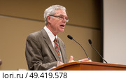 A man standing at a podium delivering a speech to an audience. He appears confident and engaged in his delivery. Стоковое AI-изображение, AI-художник Данила Большаков / Фотобанк Лори