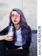 Happy beautiful teen with pink sunglasses drinks and enjoys a pink beverage sitting on urban ground. Стоковое фото, агентство Ingram Publishing / Фотобанк Лори