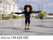 Young fit black woman on roller skates riding outdoors on urban street with open arms. Smiling girl with afro hairstyle rollerblading on sunny day. Стоковое фото, агентство Ingram Publishing / Фотобанк Лори